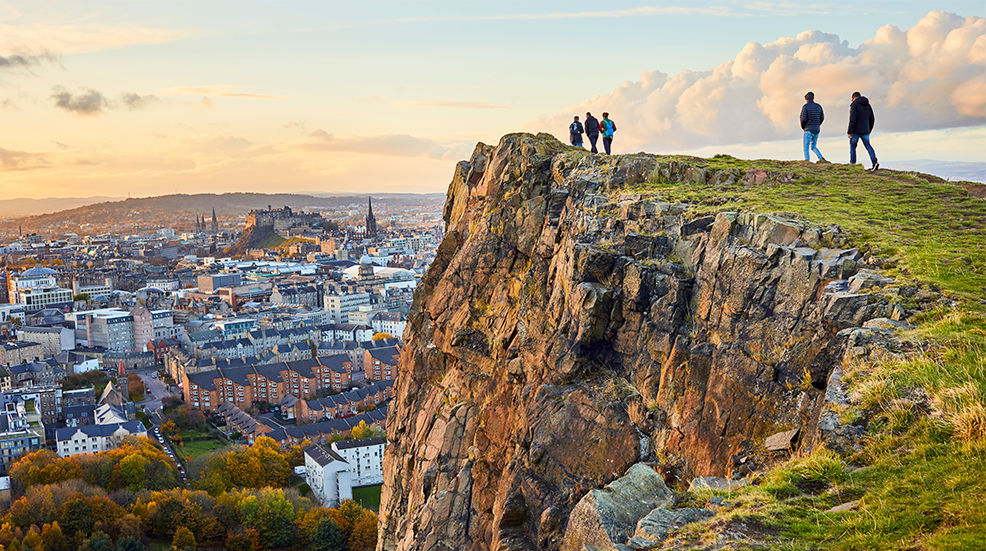 Group of people walking along cliff edge  Salisbury Crags, Holyrood Park looking at city views of Edinburgh